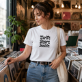 Woman in a record shop wearing a white 'Thrift Store Junkie' t-shirt in retro lettering