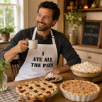 Man in a white 'I Ate All The Pies' apron at a kitchen table laden with pies