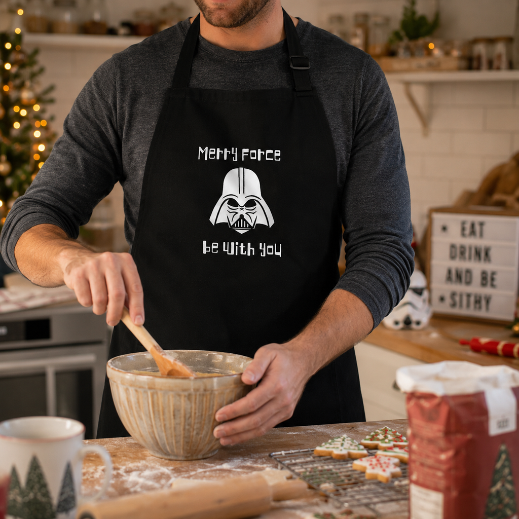 Festive black apron printed with 'Merry Force Be With You' and a geeky sci-fi helmet motif