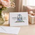 Mother's Day card with two hugging penguins reading 'Mother's Love', beside spring flowers