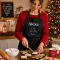 Personalised black apron reading 'Alexa Cook Christmas dinner', worn baking gingerbread in a festive kitchen