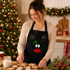 Black Christmas apron with a sparkly reindeer face, antlers, holly and red nose, worn baking biscuits