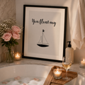Framed monochrome print reading 'You Float My' above a small sailboat, on a bathroom ledge