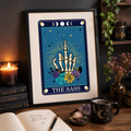 Framed tarot style print 'The Sass' with skeleton hand rude gesture and flowers, on a desk