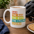 White mug with colourful 'Dad The Man The Myth The Cycling Legend' design, beside a cycle helmet