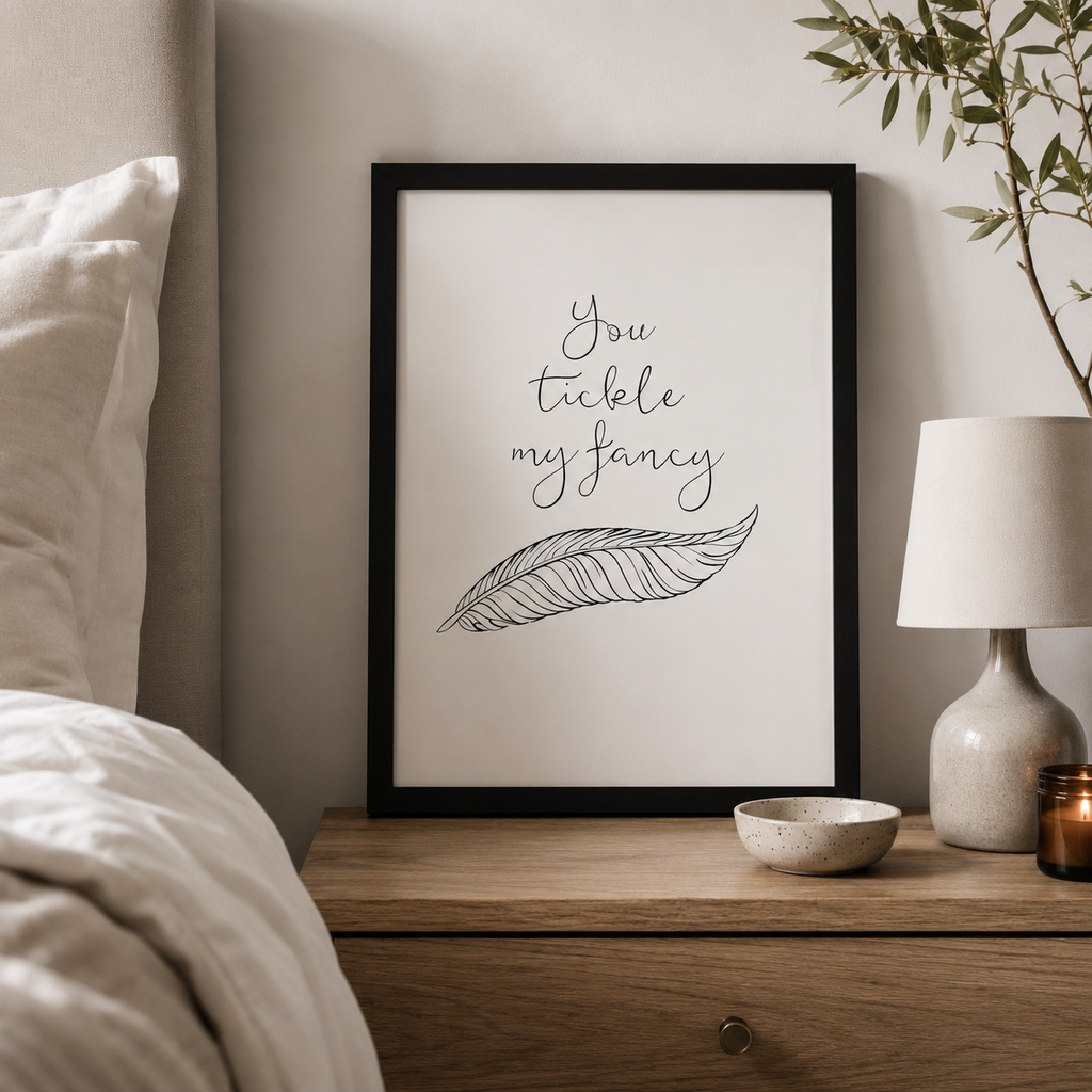 'You tickle my fancy' print with a hand-drawn feather in a black frame by a bed