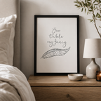 'You tickle my fancy' print with a hand-drawn feather in a black frame by a bed