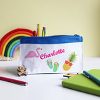 A personalized blue pencil case with white text, featuring a flamingo, pineapple, and eraser illustrations, with 'Charlotte' printed on the front.