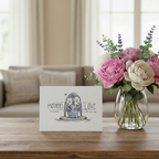 Card with penguin illustration and flowers on a table