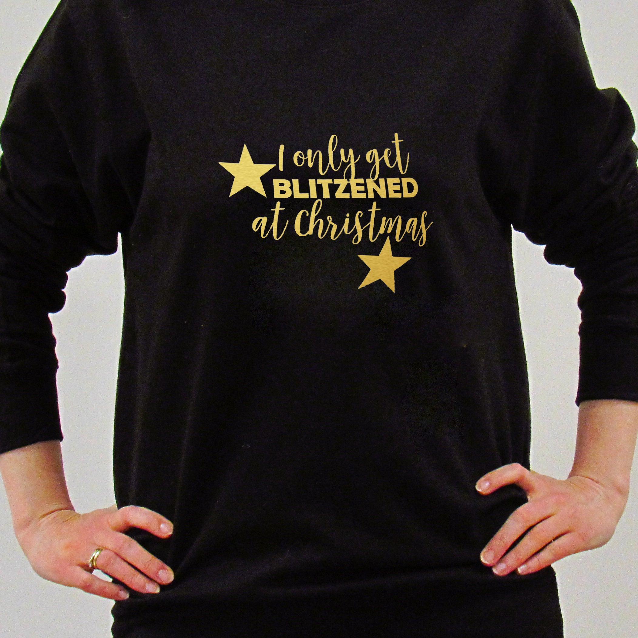 A person wearing a black Christmas jumper with the text 'I only get Blitzed at Christmas' in gold, along with gold stars and a reindeer graphic.