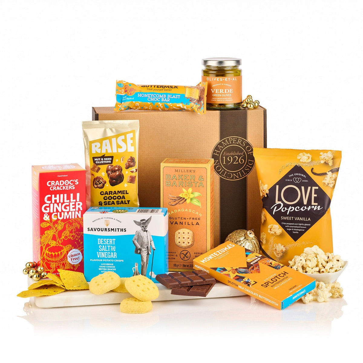 Gluten Free Hamper with olives, chilli ginger crackers, crisps, vanilla popcorn, biscuits and chocolate in front of a kraft gift box