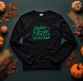 Black sweatshirt with a green glow design reading 'Happy Hallo Wine', laid flat among pumpkins and autumn leaves