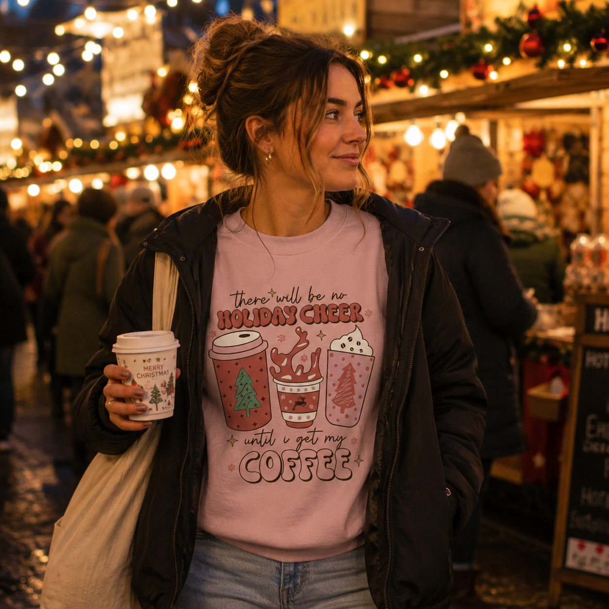 Woman at a Christmas market holding a coffee cup wearing a pink festive coffee slogan sweatshirt