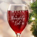 Personalised I'm on the Naughty List wine glass filled with red wine by the Christmas tree