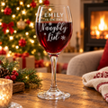 Personalised I'm on the Naughty List wine glass filled with red wine by the Christmas tree
