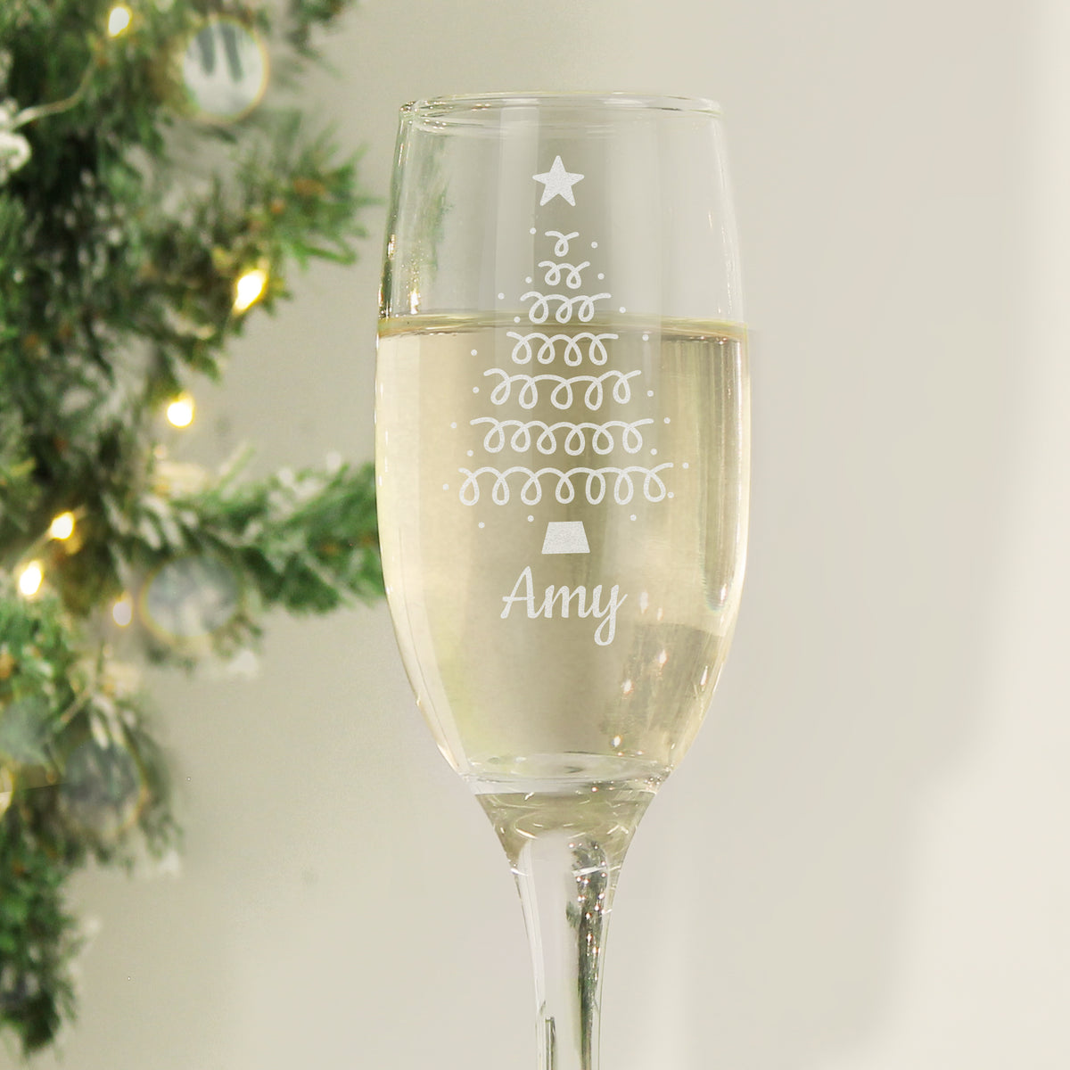 Personalised Christmas tree champagne flute with a name, beside a Christmas tree