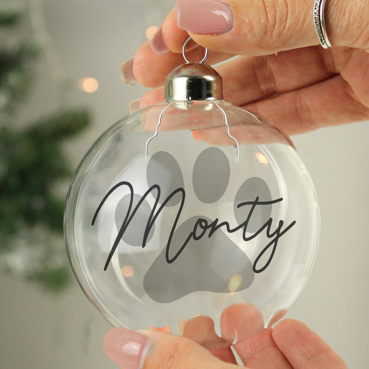 Personalised paw print glass Christmas bauble glowing on a lit tree