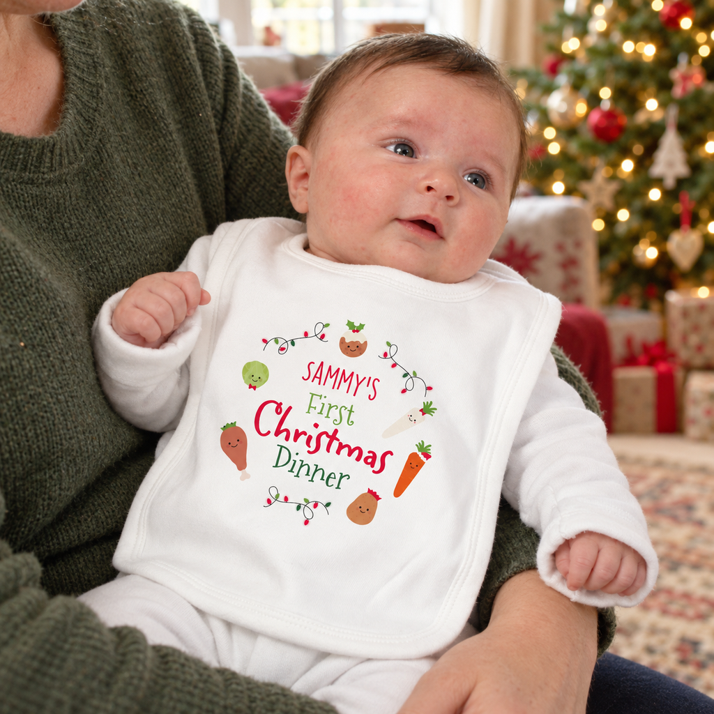 Baby wearing a personalised First Christmas Dinner bib by the Christmas tree