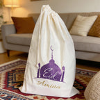 White drawstring bag with 'Eid Mubarak Amina' design on a rug in a living room.