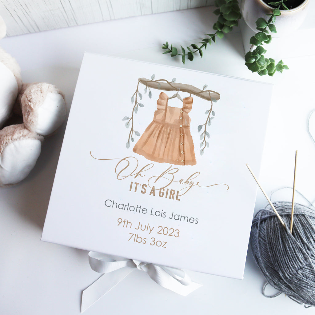 A personalized white luxury baby gift box with hand-drawn illustration, a watercolour bear design, and the name 'Charlotte it's a girl' written on it, alongside some knitting yarn and scissors.