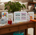 Collection of birthday cards on a wooden table with a plant and gift in the background