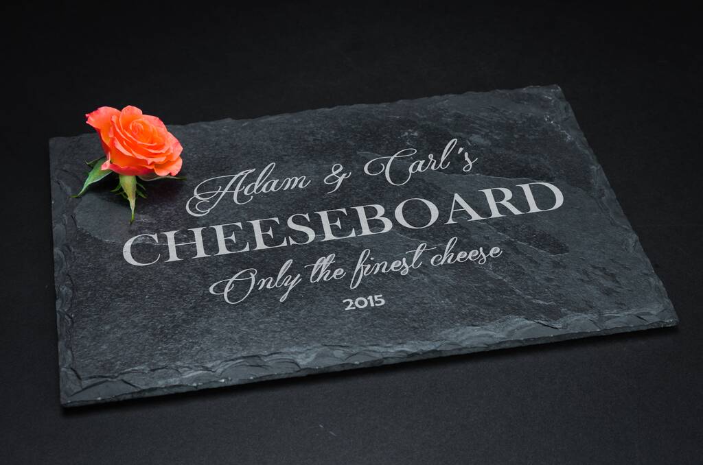 Personalised slate cheeseboard in a cosy lifestyle setting, surrounded by wine, crackers, olives and cheese.