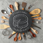 Personalised slate serving board surrounded by wooden spoons, spatulas and other cooking accessories.