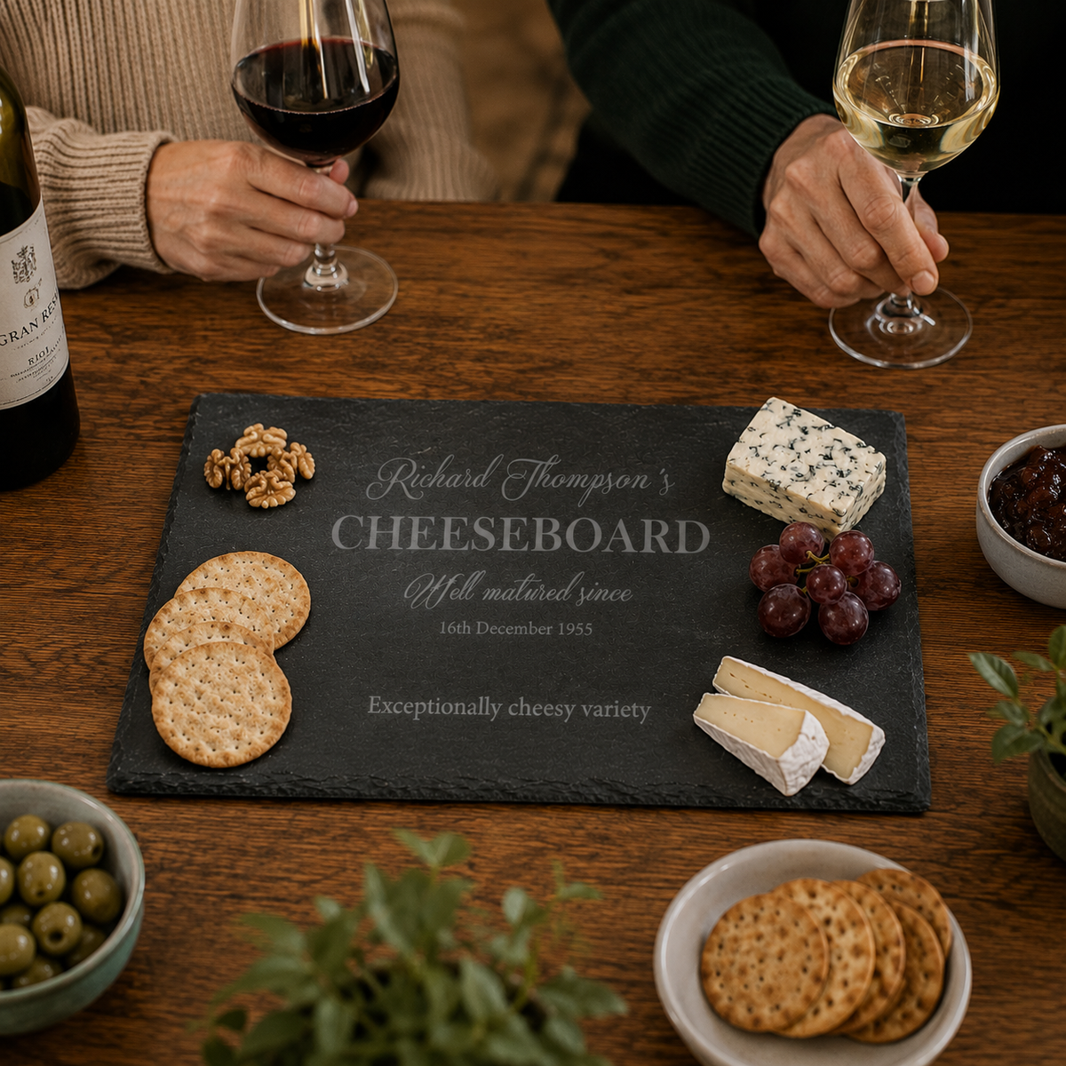 Rectangular black slate cheeseboard with personalised engraving, displayed on a wooden dining table.