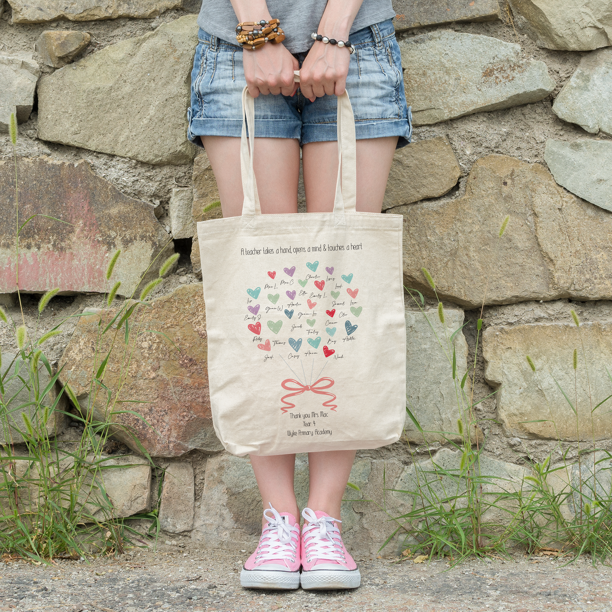A person holding a beige tote bag with a heart pattern and a personalized message that reads 'Thank you for being such an inspiring teacher. The world needs more educators like you.