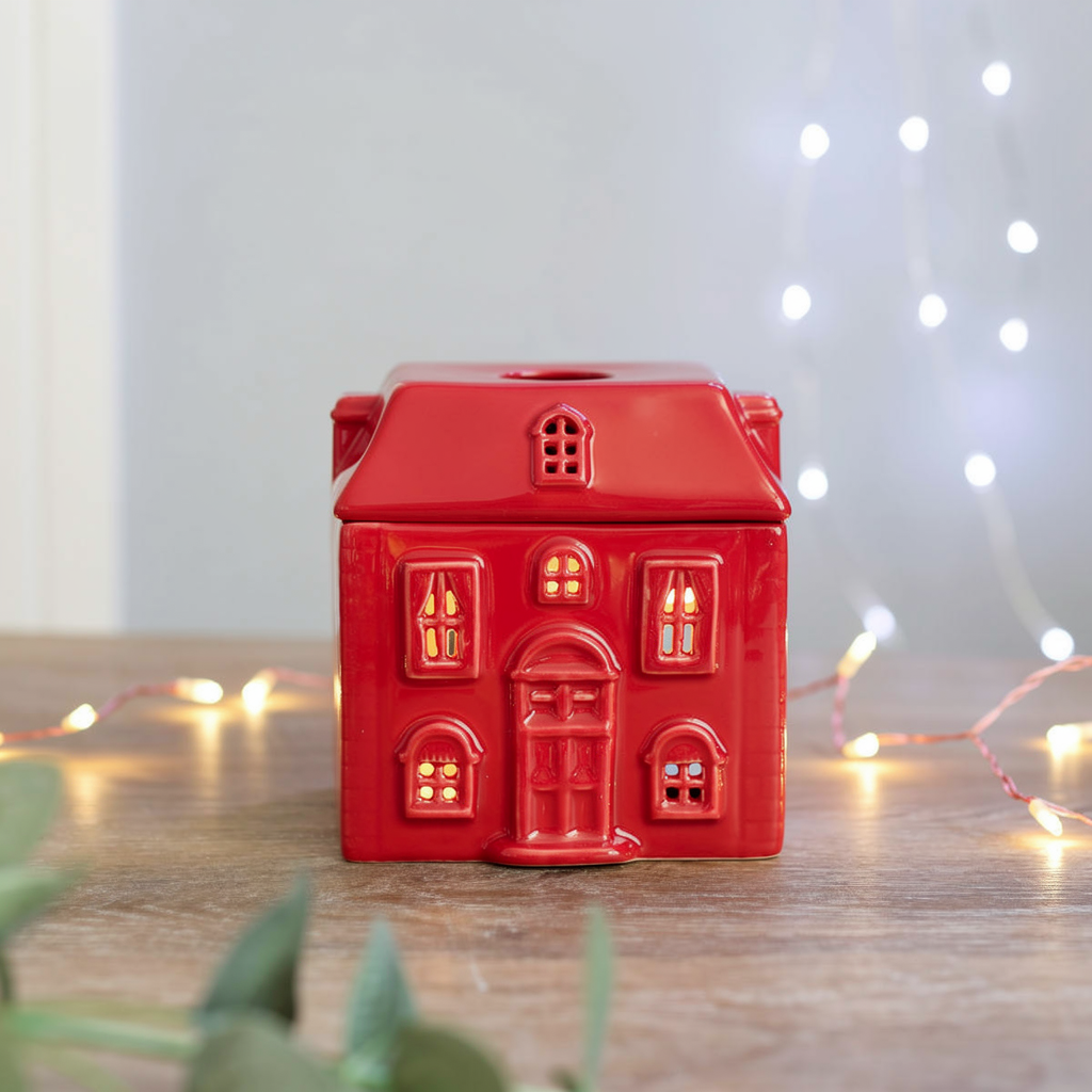 Red house-shaped candle on a wooden surface with string lights in the background