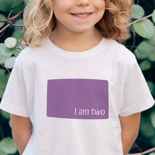 Child wearing a white birthday t-shirt with a purple panel reading 'I am two'