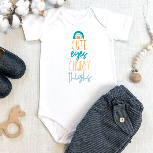 White baby grow with rainbow design reading 'Cute eyes chubby thighs'
