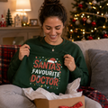 Woman opening a gift box wearing a green Santa's Favourite Doctor Christmas sweatshirt