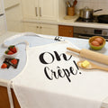 Cream 'Oh Crepe!' baking apron on a kitchen worktop with strawberries, eggs and a rolling pin