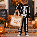 Child in a skeleton Halloween costume holding a jute trick or treat bag personalised with the name 'Jack', on a porch with carved pumpkins.