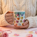 Hands holding a 3D-effect mug covered in colourful love heart sweets