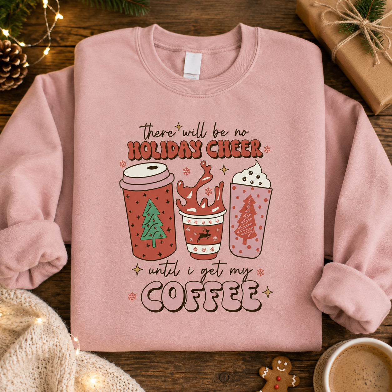 Pink Holiday Cheer coffee slogan Christmas sweatshirt laid flat with pine cones and a gift box