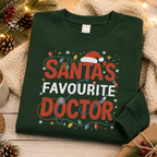 Green Santa's Favourite Doctor Christmas sweatshirt folded with pine cones and a cosy throw