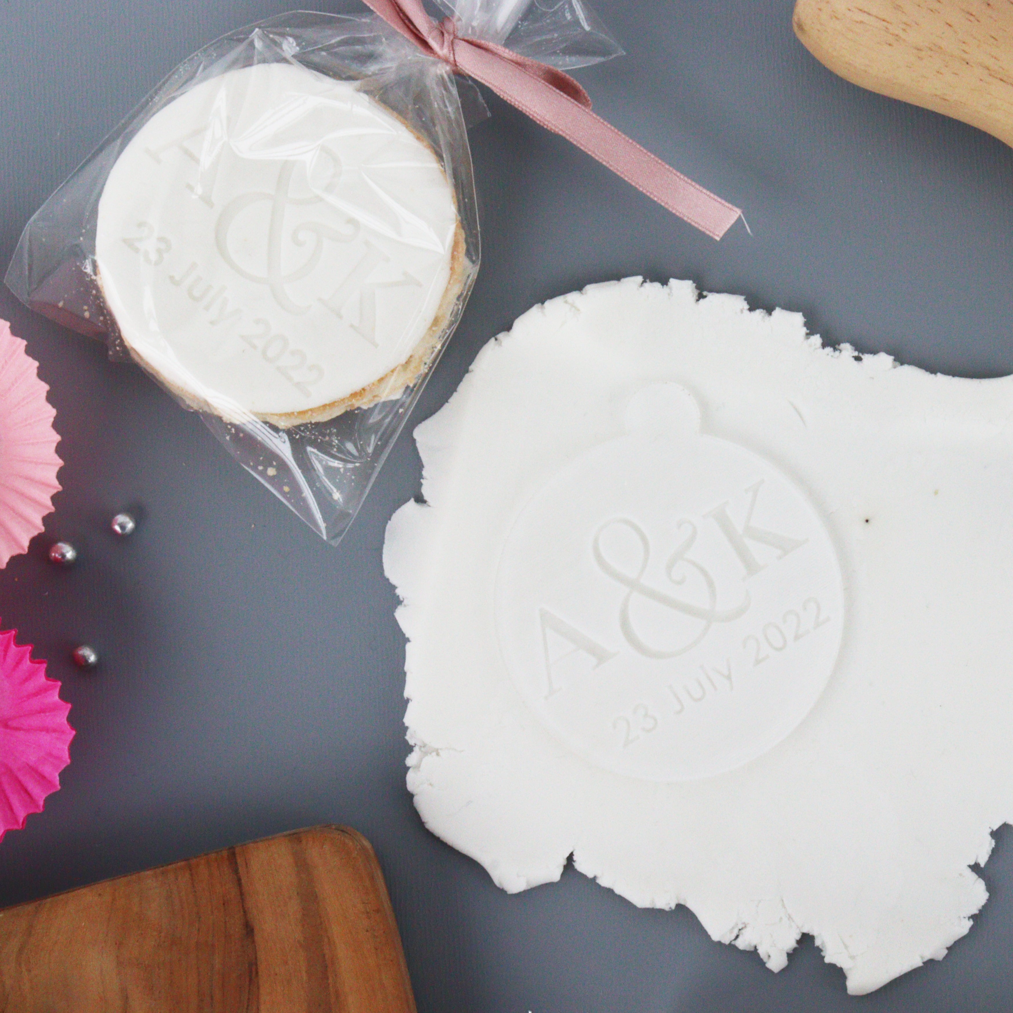An acrylic cookie press with a personalized embossed design, engraved with a laser, displaying a fondant embosser with a couple's initials.