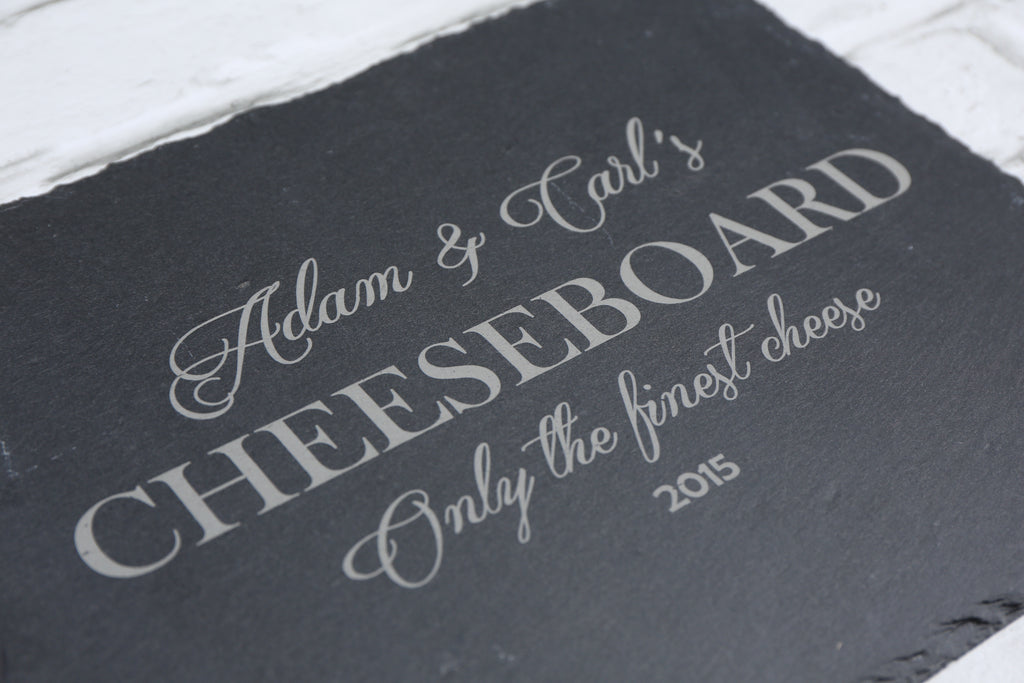 Engraved slate cheeseboard presented in a relaxed dining setting with wine and sharing snacks.