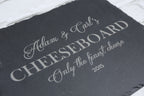 Engraved slate cheeseboard presented in a relaxed dining setting with wine and sharing snacks.