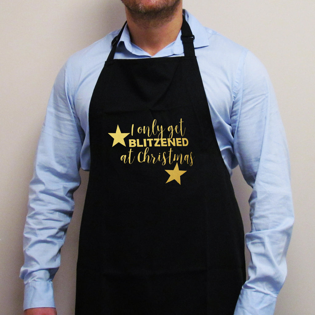 Black apron with 'I Only Get Blitzened at Christmas' in gold stars on the front, worn by a person