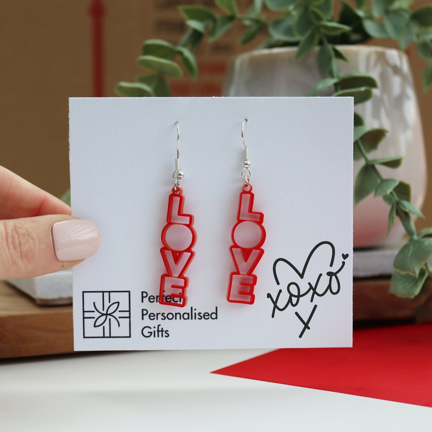 LOVE laser cut red acrylic valentines earrings dangly earrings with the word LOVE in a vertical direction shown by a hand holding the backing gift card