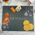 A natural slate cheeseboard with a Christmas-themed design, featuring engravings of a reindeer, snowflakes, and the name 'The Peakers'.