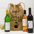 A burlap wine gift bag with 'Amelia is on Santa's Good List' text and a cute snowman illustration, alongside three wine bottles.