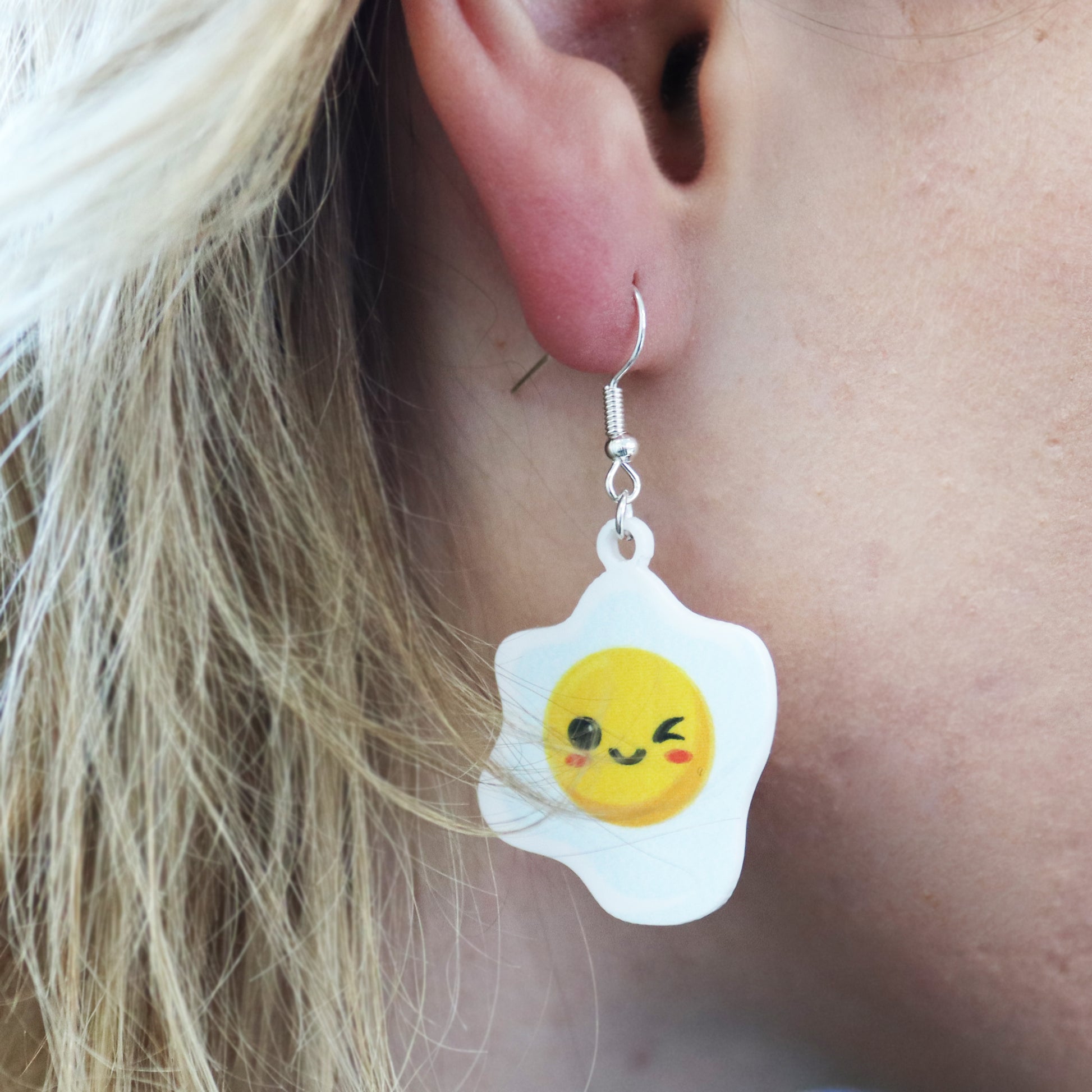 bacon to my eggs earrings shown on a white and yellow background egg shown in ear
