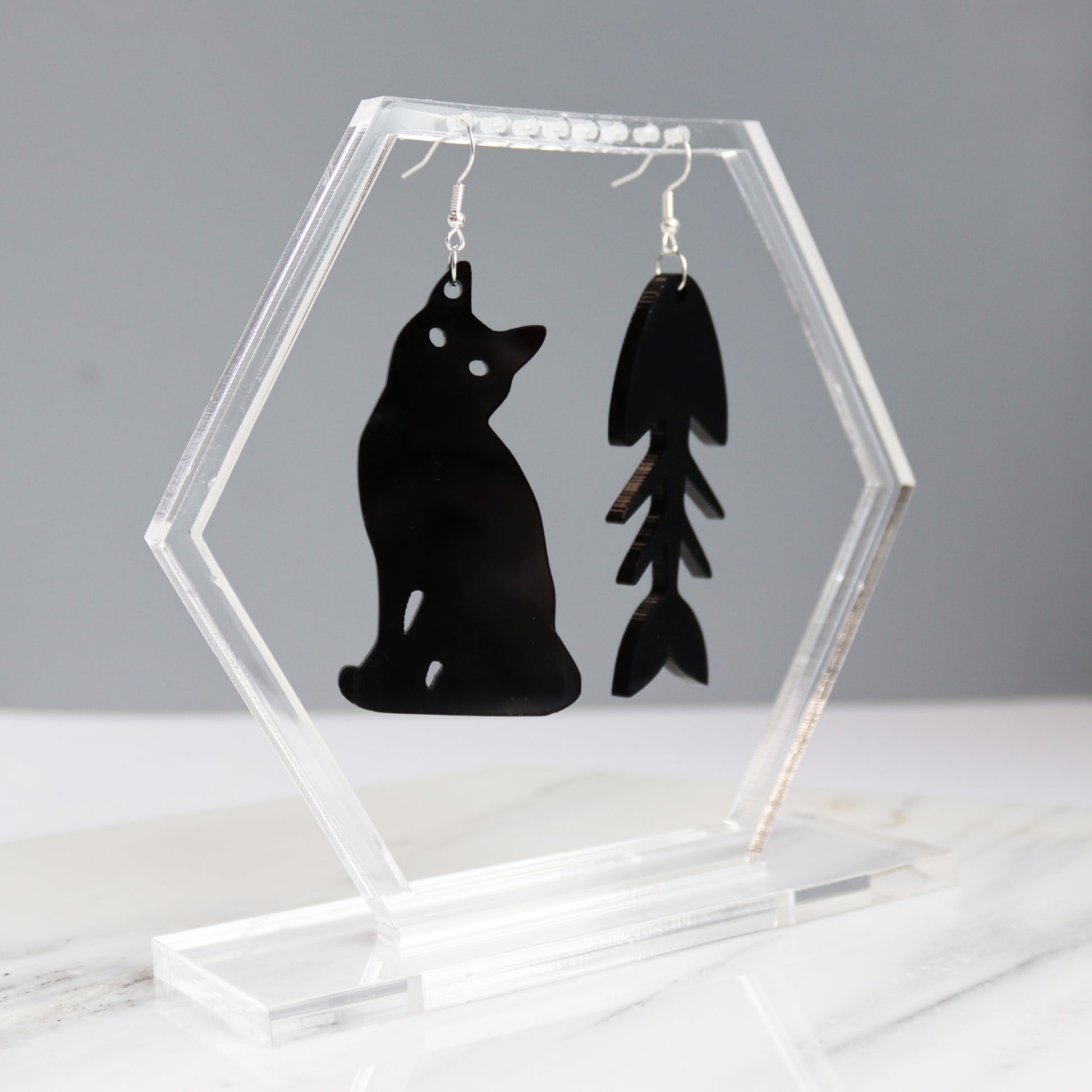 black cat and fish bone mismatches earrings cut from black acrylic shown hanging on earring display holder