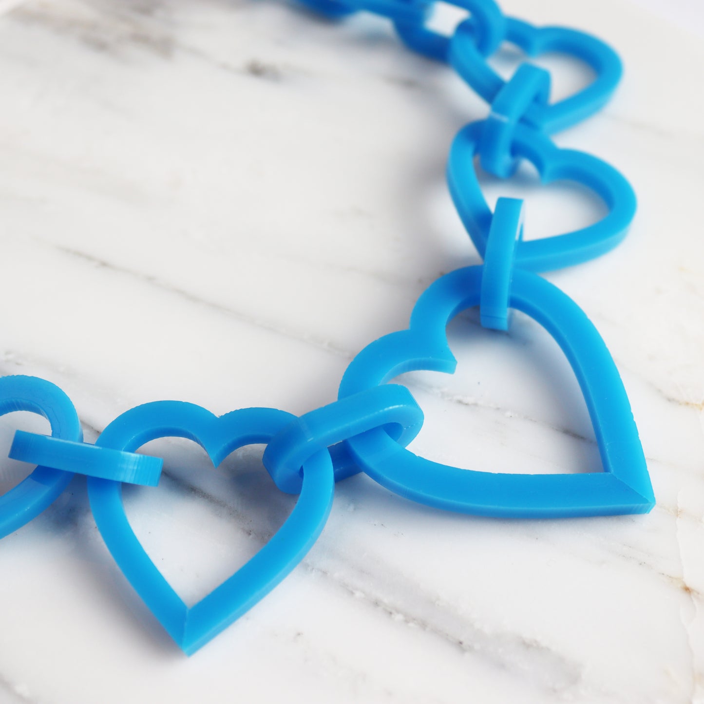 blue statement heart acrylci necklace close up shown on marble background