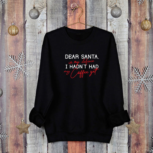 Black Christmas jumper reading 'Dear Santa, in my defence I hadn't had my coffee yet', on a hanger