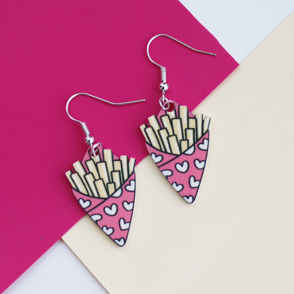 fries before guys earrings cut from acrylic and printed with a bag of chips design the bag of chips is pink and has hearts printed on it